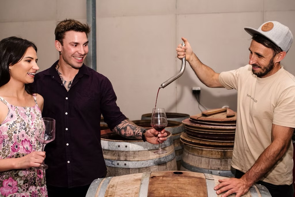 A Barossa winemaker drawing red wine from the barrel for two guests at a cellar tasting