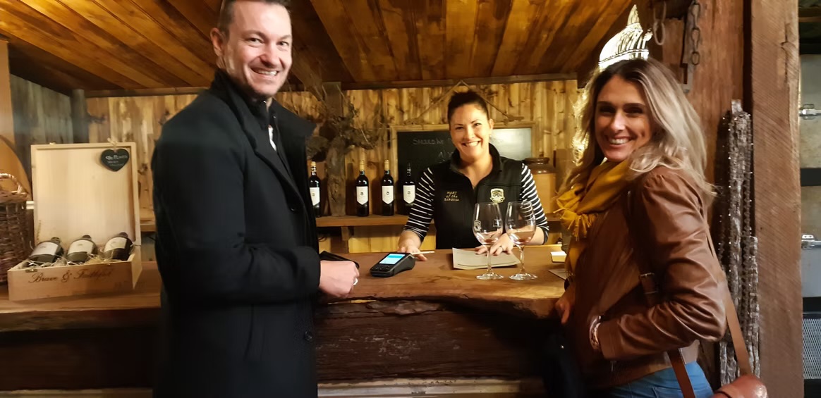 Two guests smiling at a timber cellar door tasting counter with their host in the Barossa